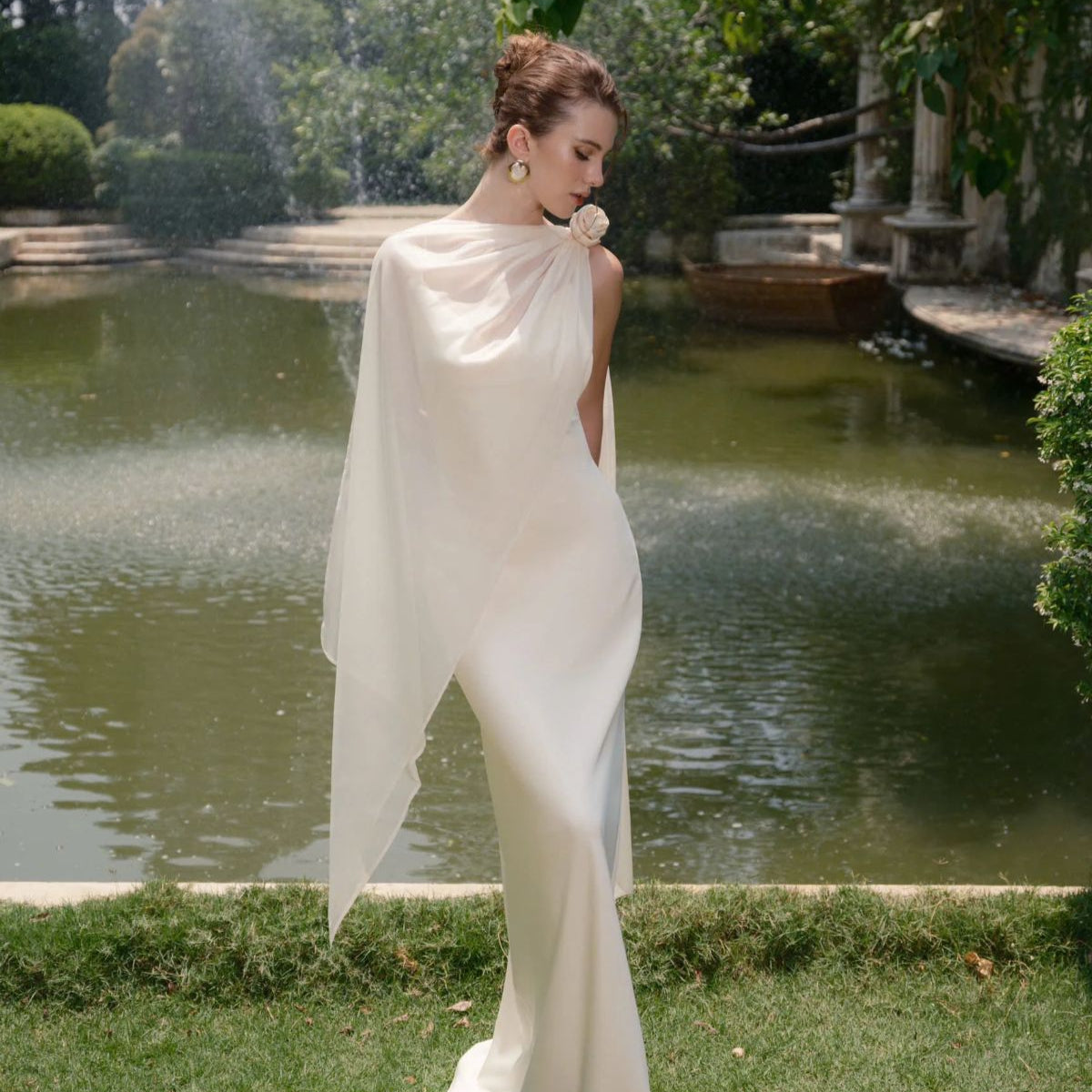 Woman in a white dress standing by a pond with greenery in the background